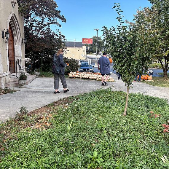 People setting out pumpkins on a sidewalk in front of a church for fall sale.