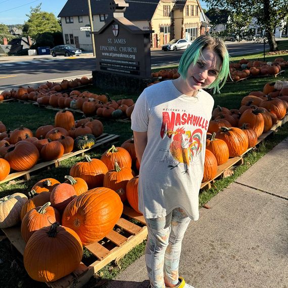 Person with teal hair in front of a pumpkin patch at a church, wearing a Nashville t-shirt.