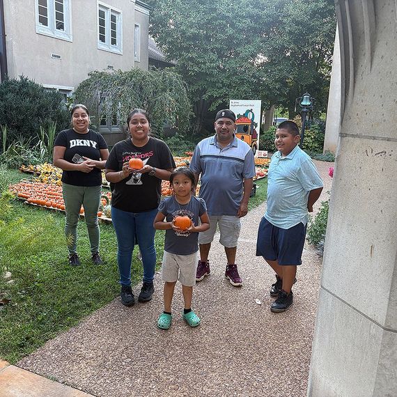 Family of five holding pumpkins outdoors.