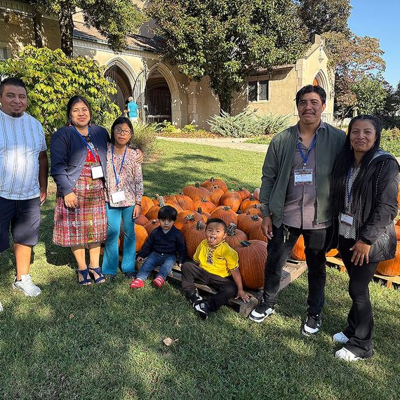 Family posing with pumpkins in front of a building. Children sitting and standing. Sunny day.