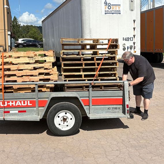 Man securing pallets on a U-Haul trailer, near a truck.