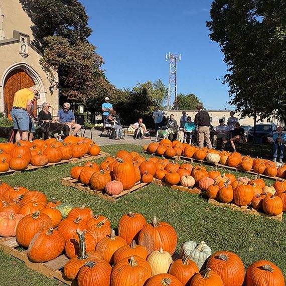 Pumpkins on display outside church, people gathered. Sunny day.