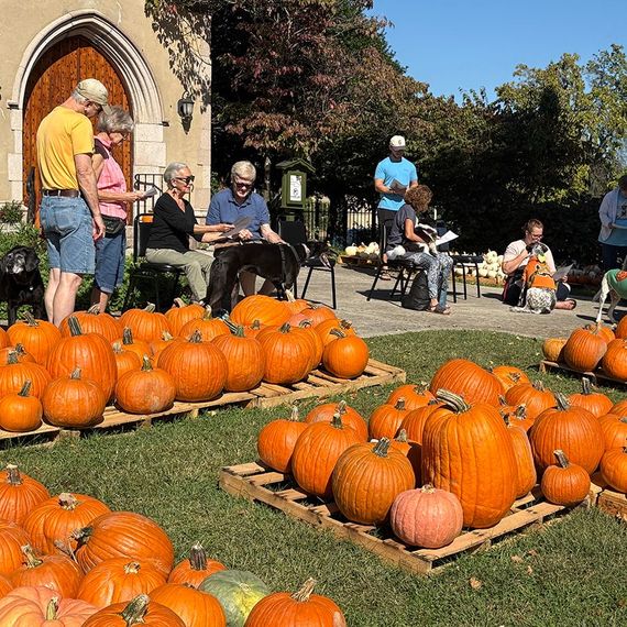 Pumpkins displayed on pallets, people shopping outside a church. Sunny day.