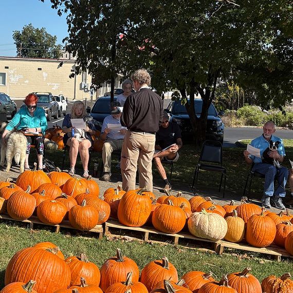 People gathered among pumpkins on a sunny day. A man holds a dog.