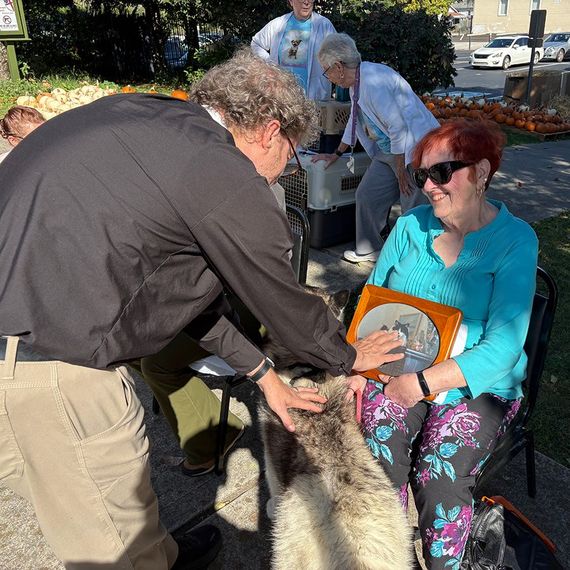 People petting a dog outdoors; woman in turquoise holding photo, other people behind.
