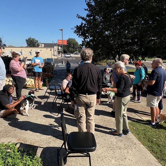 Group of people outdoors, some with dogs, gathered on a sunny day.