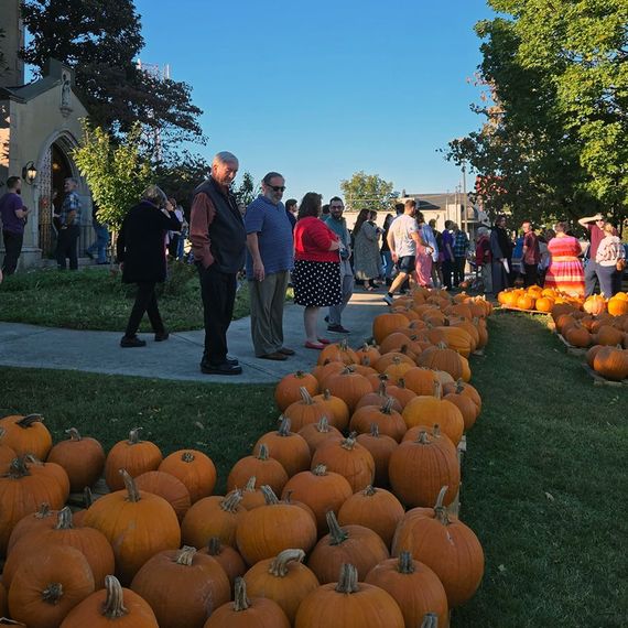 People gather near pumpkins in front of a church on a sunny day.