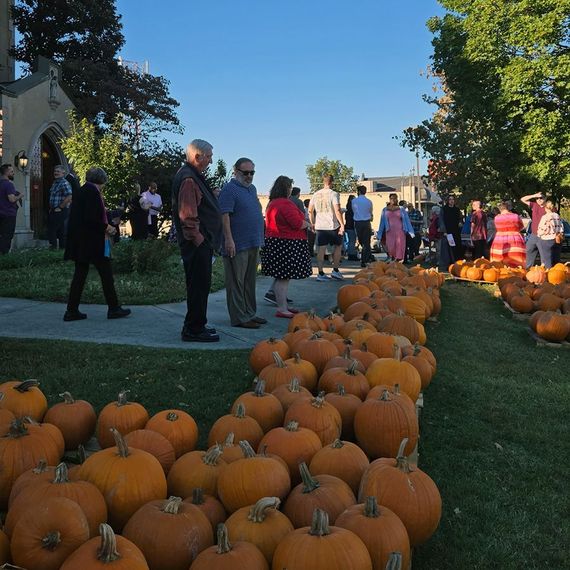 People gather around a large display of pumpkins outside a church.