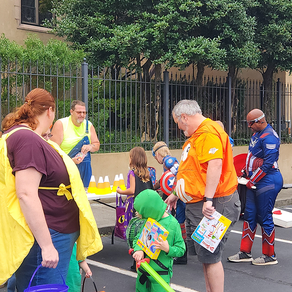 People in costumes at a table; Captain America, a ninja, and others pose. Outdoor daytime scene with a fence and trees.