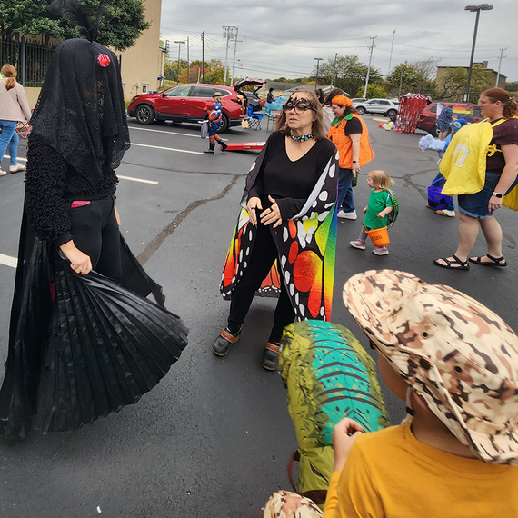 People in costumes at an outdoor event, including a person wearing a butterfly cape and another in a black outfit.
