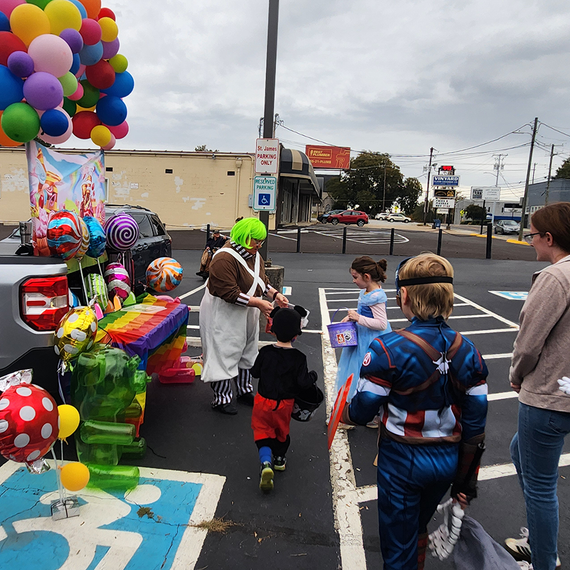 Children in costumes trick-or-treating at a trunk-or-treat event, clown handing out candy.