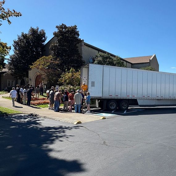 People line up next to a semi-truck outside a church on a sunny day.