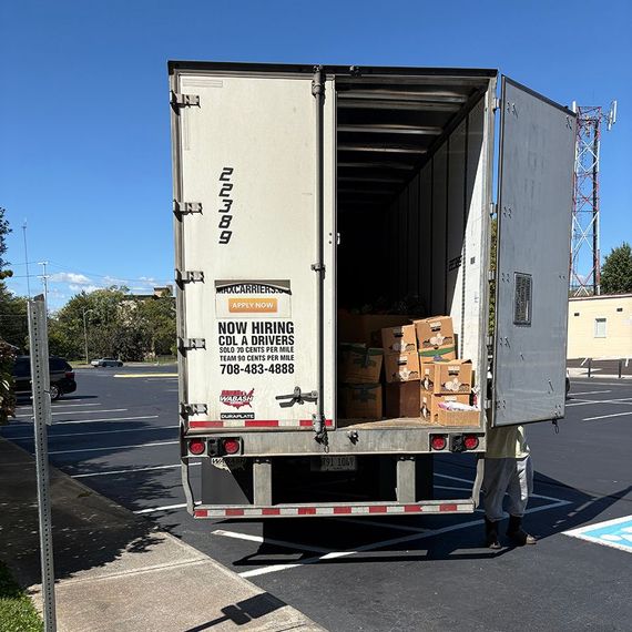 Rear view of a white semi-truck trailer with open doors, containing boxes. Parking lot setting.