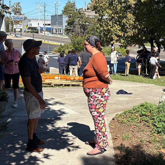 Two people talking outside near pumpkins, other people in the background.