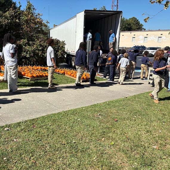 Students unload pumpkins from a truck outdoors on a sunny day.