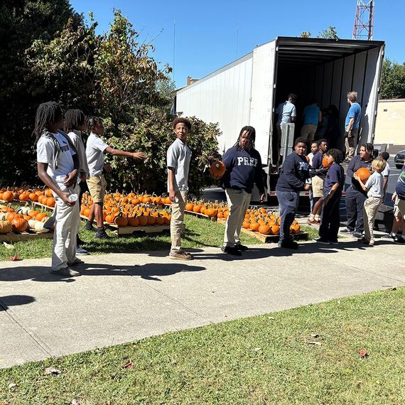 Children unloading pumpkins from a truck; many pumpkins on the ground.
