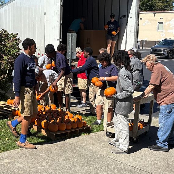 People unloading pumpkins from a truck, some holding them. Outdoors, sunny day.