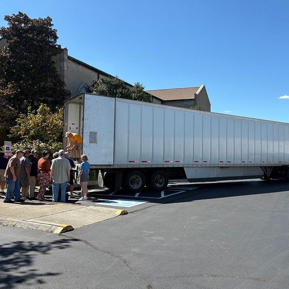 People loading a semi-trailer outside a building on a sunny day.