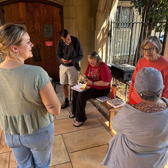 Group of people outside, some smiling, others looking at things. One person is writing, another taking a photo.