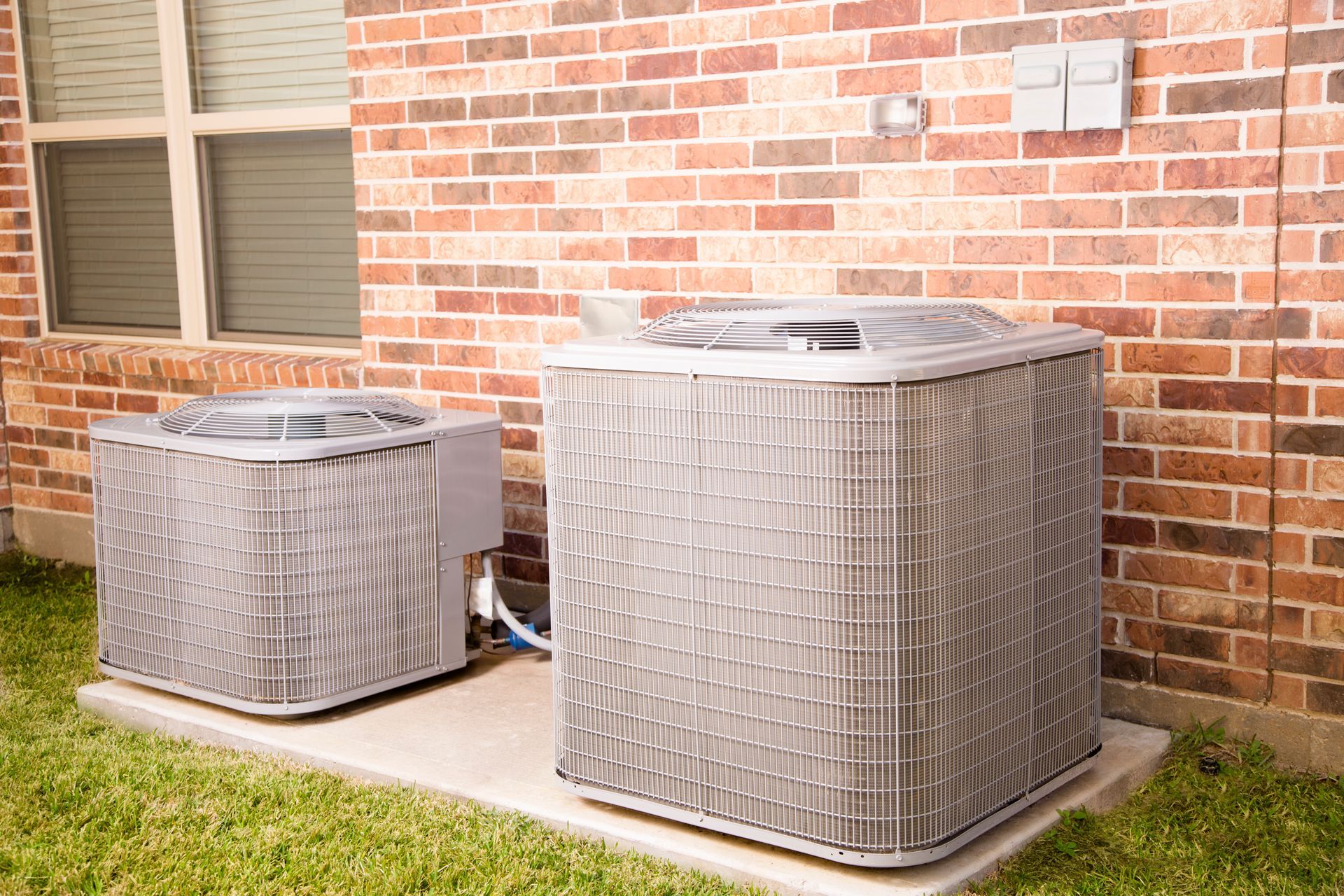 Two air conditioners are sitting outside of a brick building.