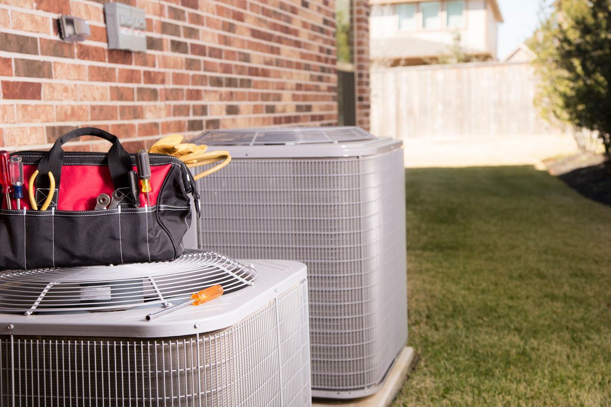 Two air conditioners are sitting next to each other on the side of a brick building installed by Conley Cooling and Heating.