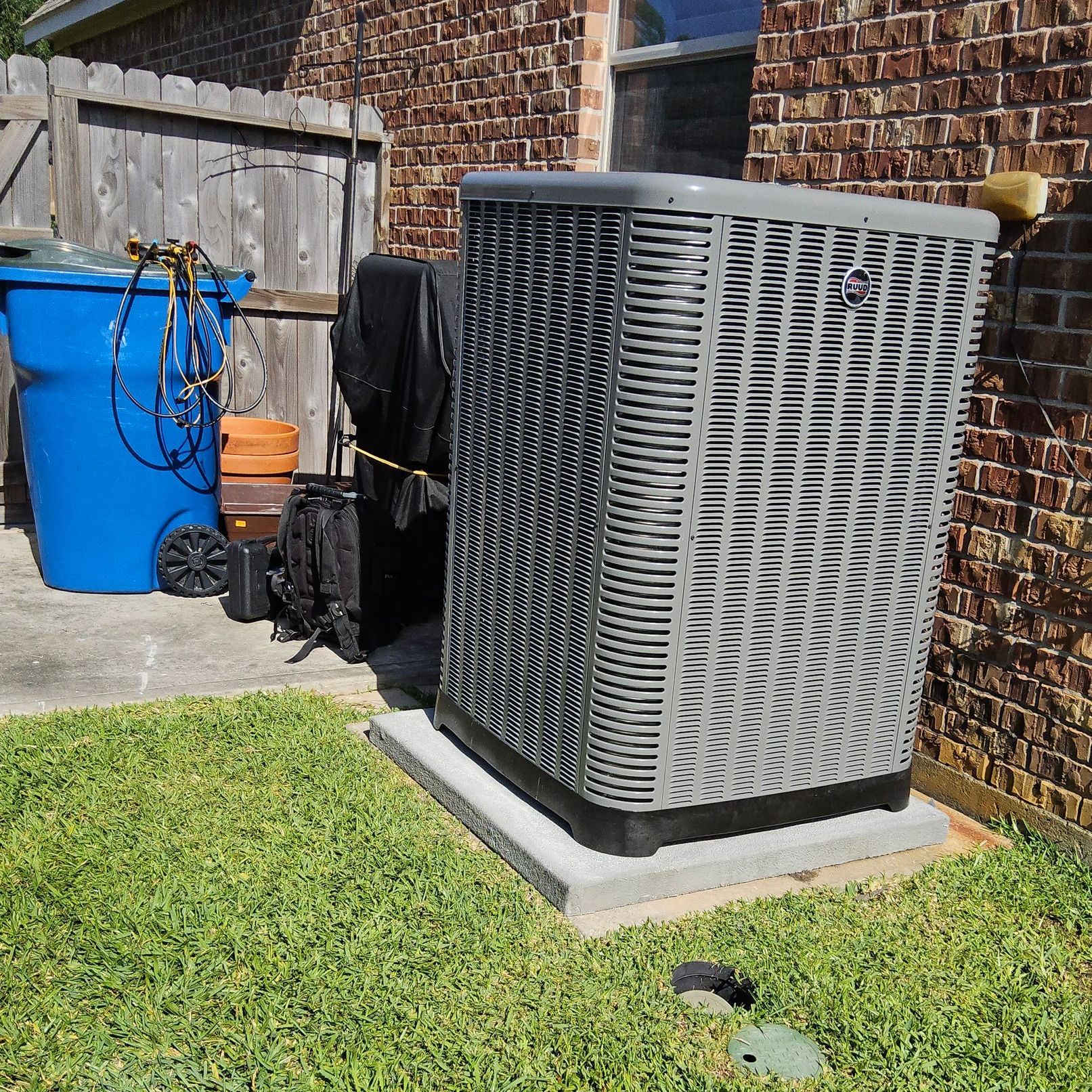 A gray air conditioner is sitting in the grass in front of a brick building.