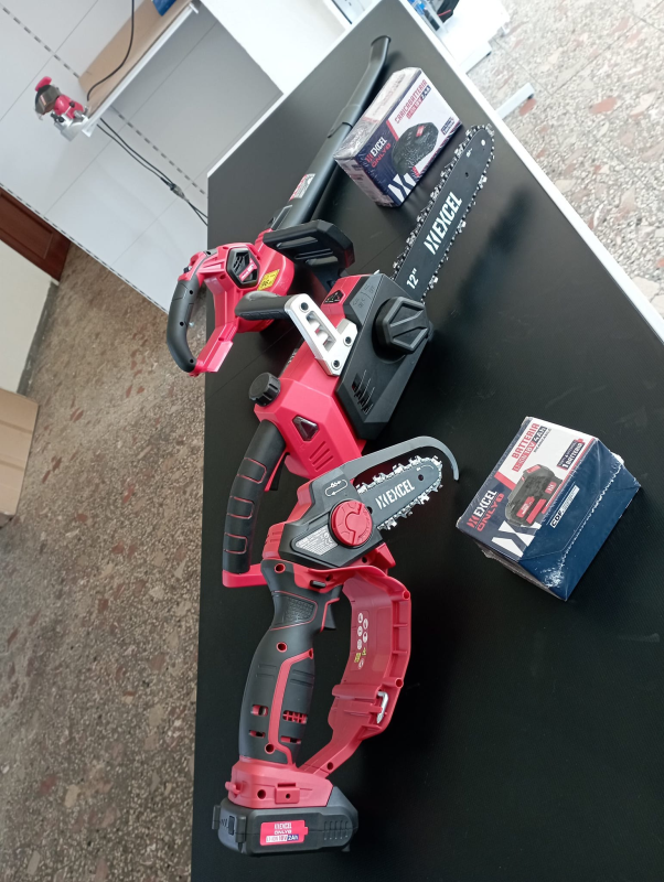 Mini motosega a batteria rossa e nera su una superficie nera con la sua scatola.