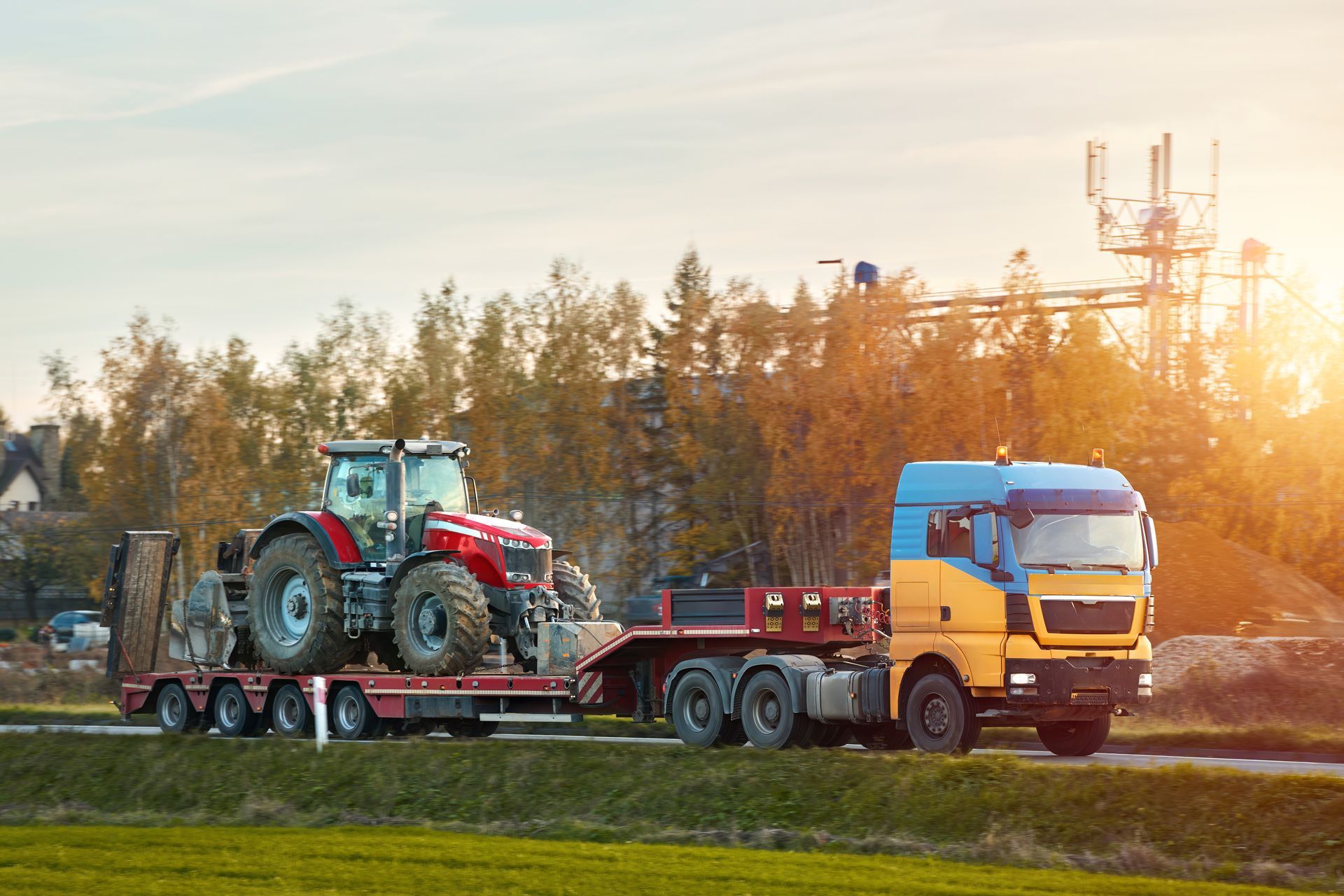 Tractor on a Flatbed Trailer Being Hauled by a Semi-truck on a Rural Road, Sunny Day