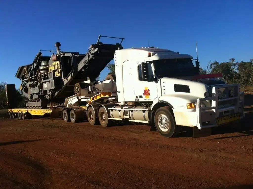 A White Semi Truck is Carrying a Large Machine — JEC Transport in Winnellie, NT