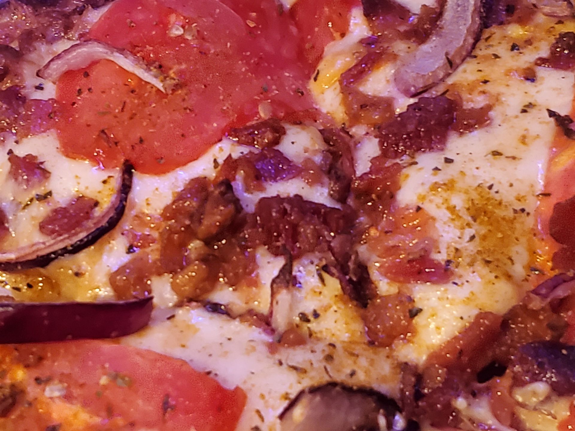 A close up of a pizza with tomatoes , onions , bacon and cheese.