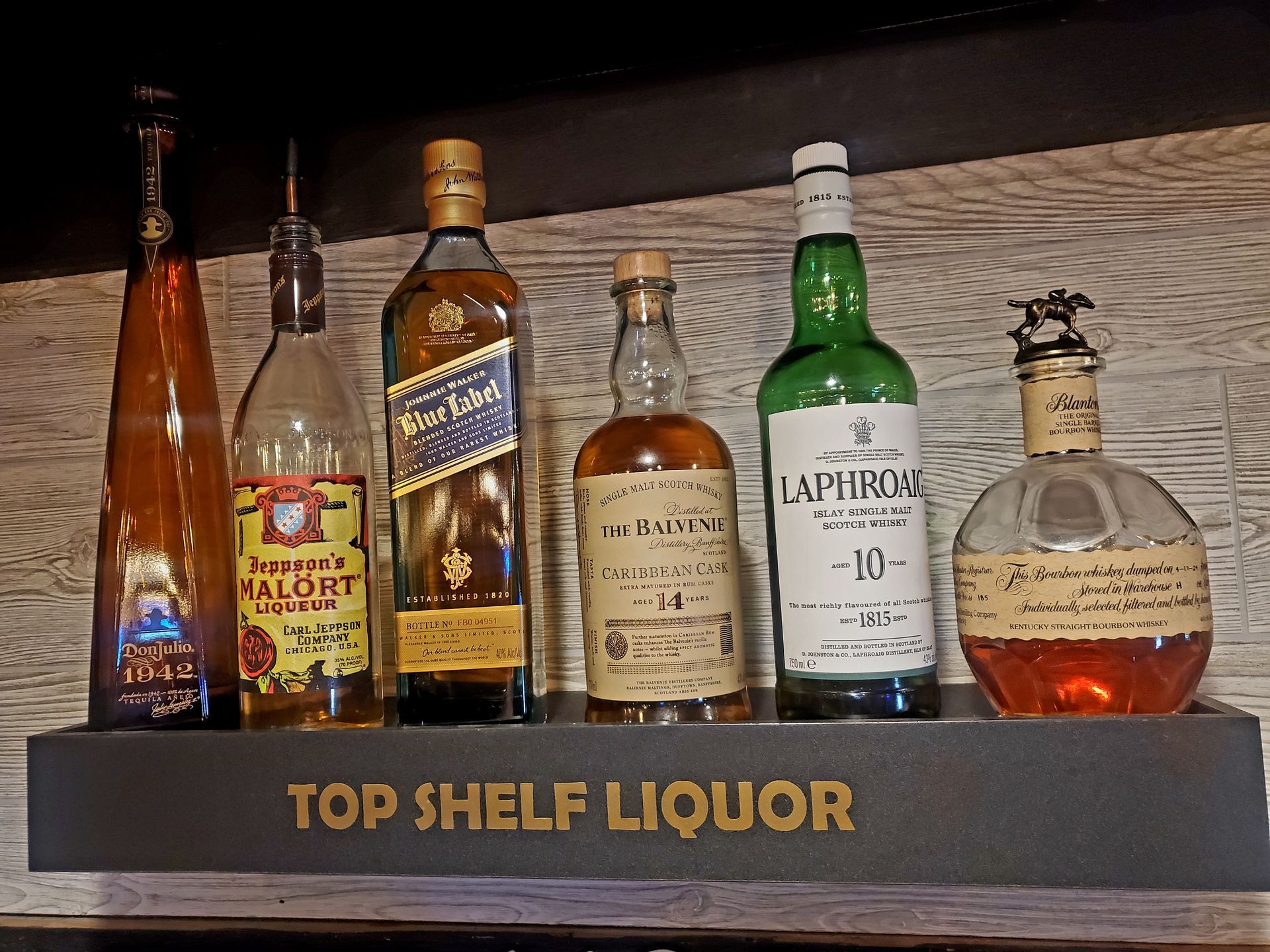Several bottles of liquor are sitting on top of a top shelf liquor shelf.