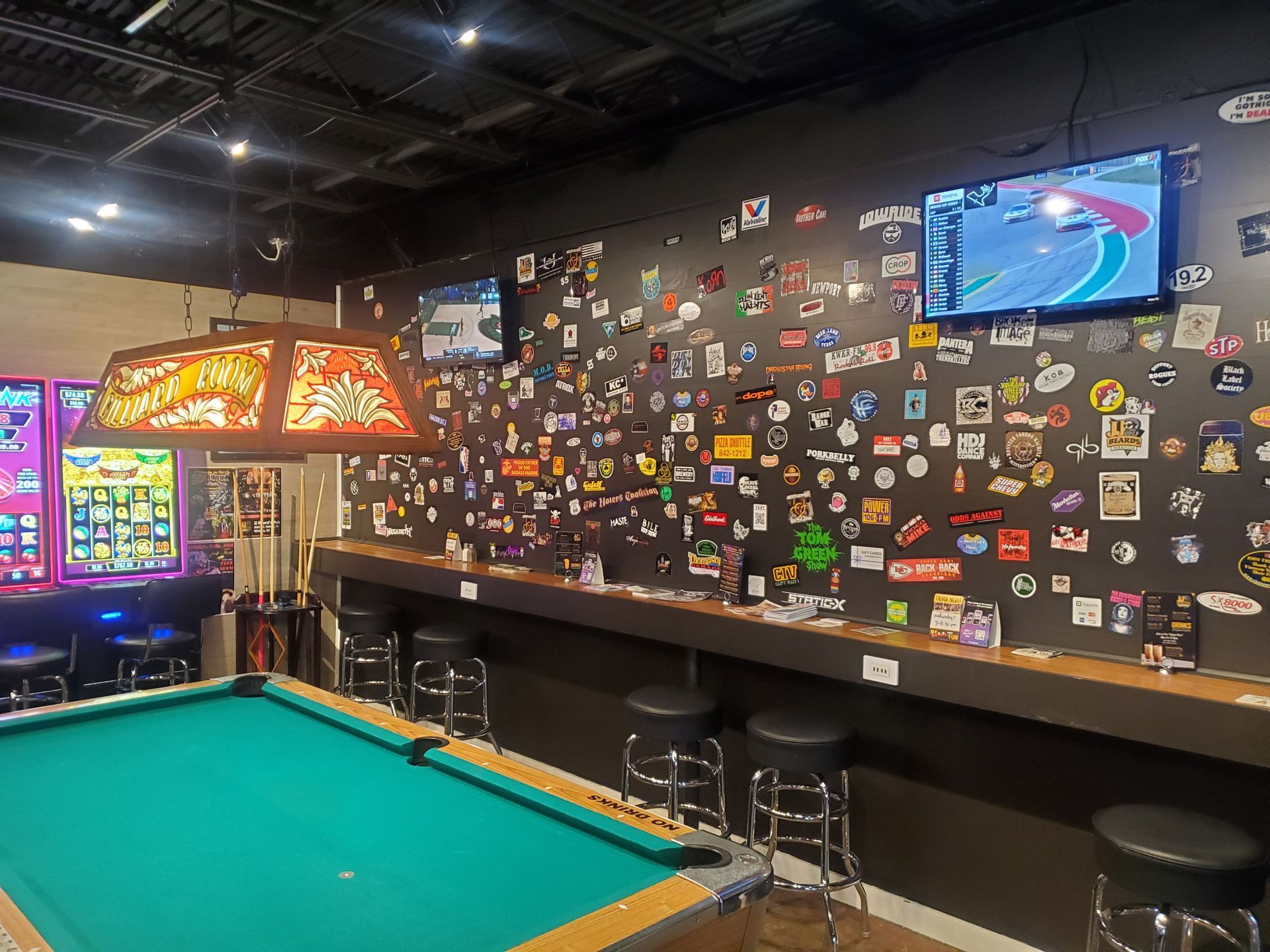 A pool table in a bar with a wall covered in stickers.