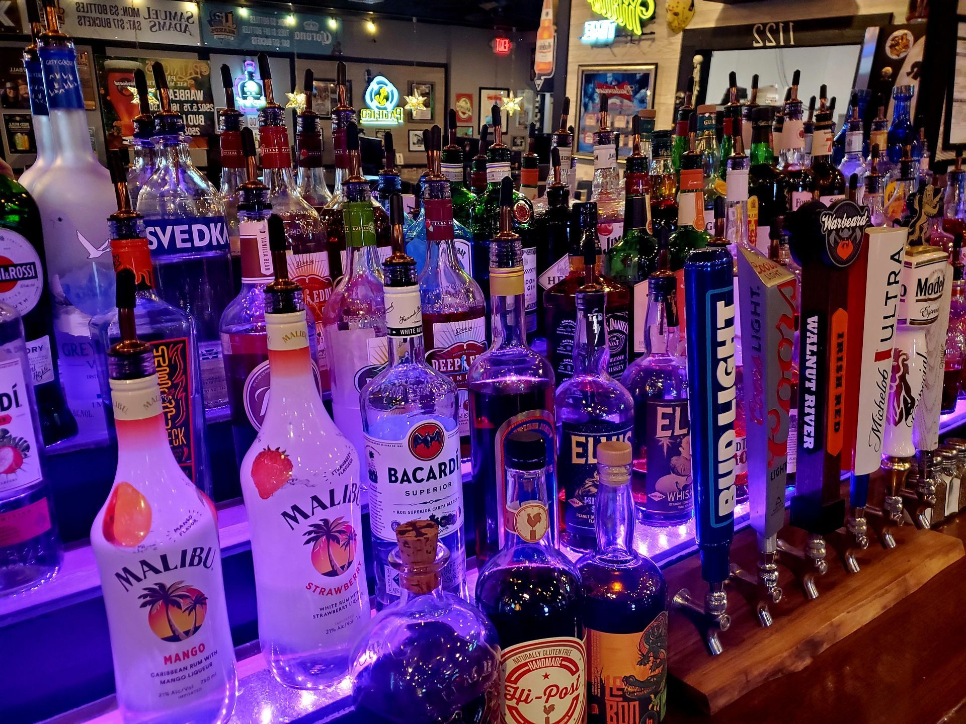 A bar filled with lots of bottles of liquor and beer taps.