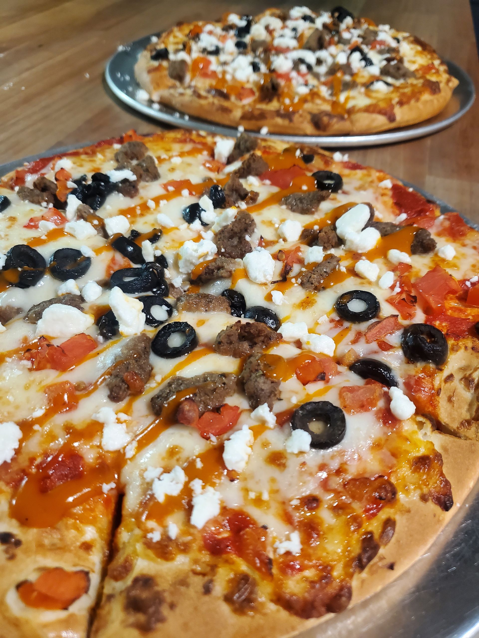 Two pizzas are sitting on a metal tray on a table.