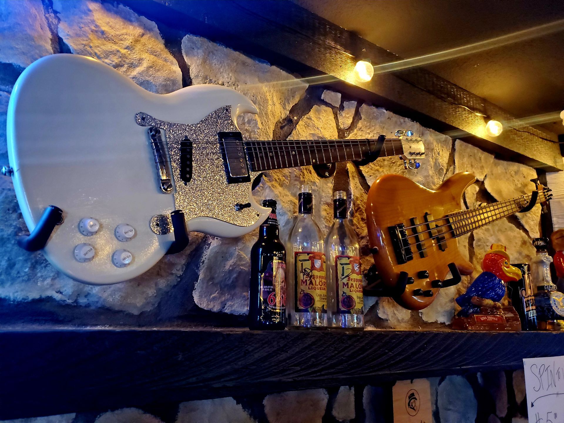 Two guitars are hanging on a wall next to bottles of alcohol.