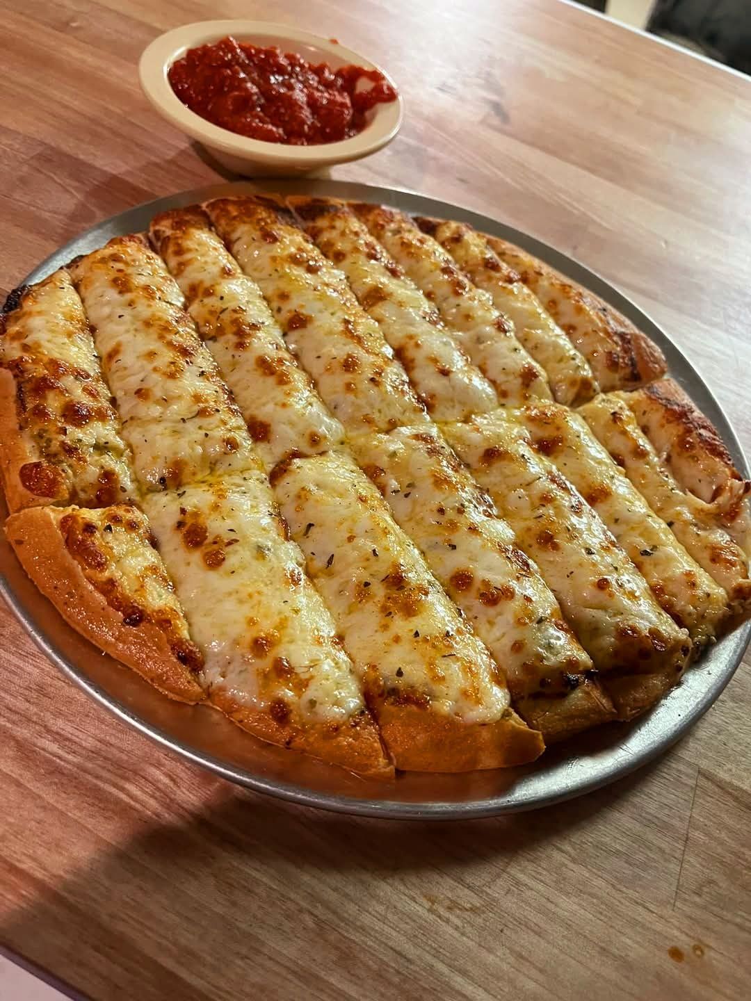 A pizza with cheese sticks and a bowl of sauce on a wooden table.