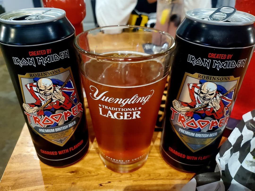 Two cans of yuengling lager and a glass of beer on a wooden table.