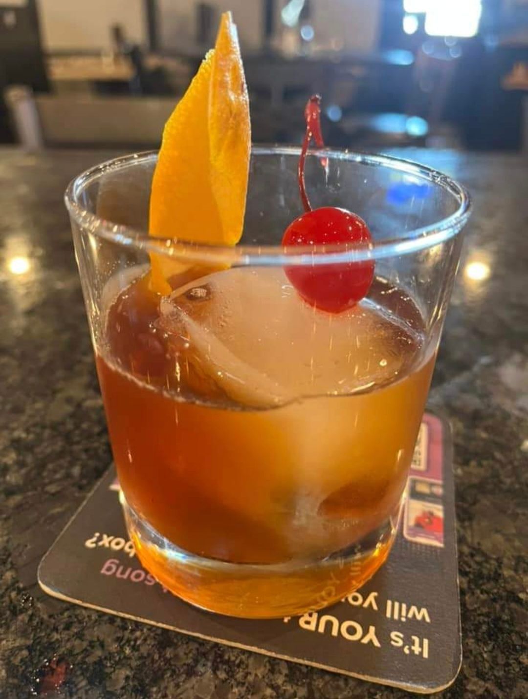 A drink with a cherry on top is on a coaster that says it 's your