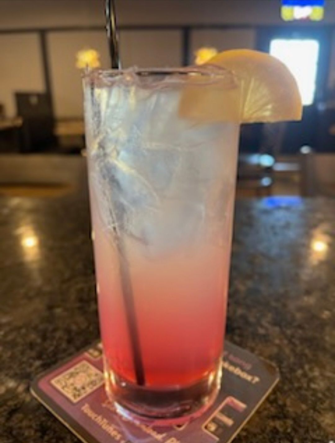 A tall glass of pink liquid with a straw and a slice of lemon.