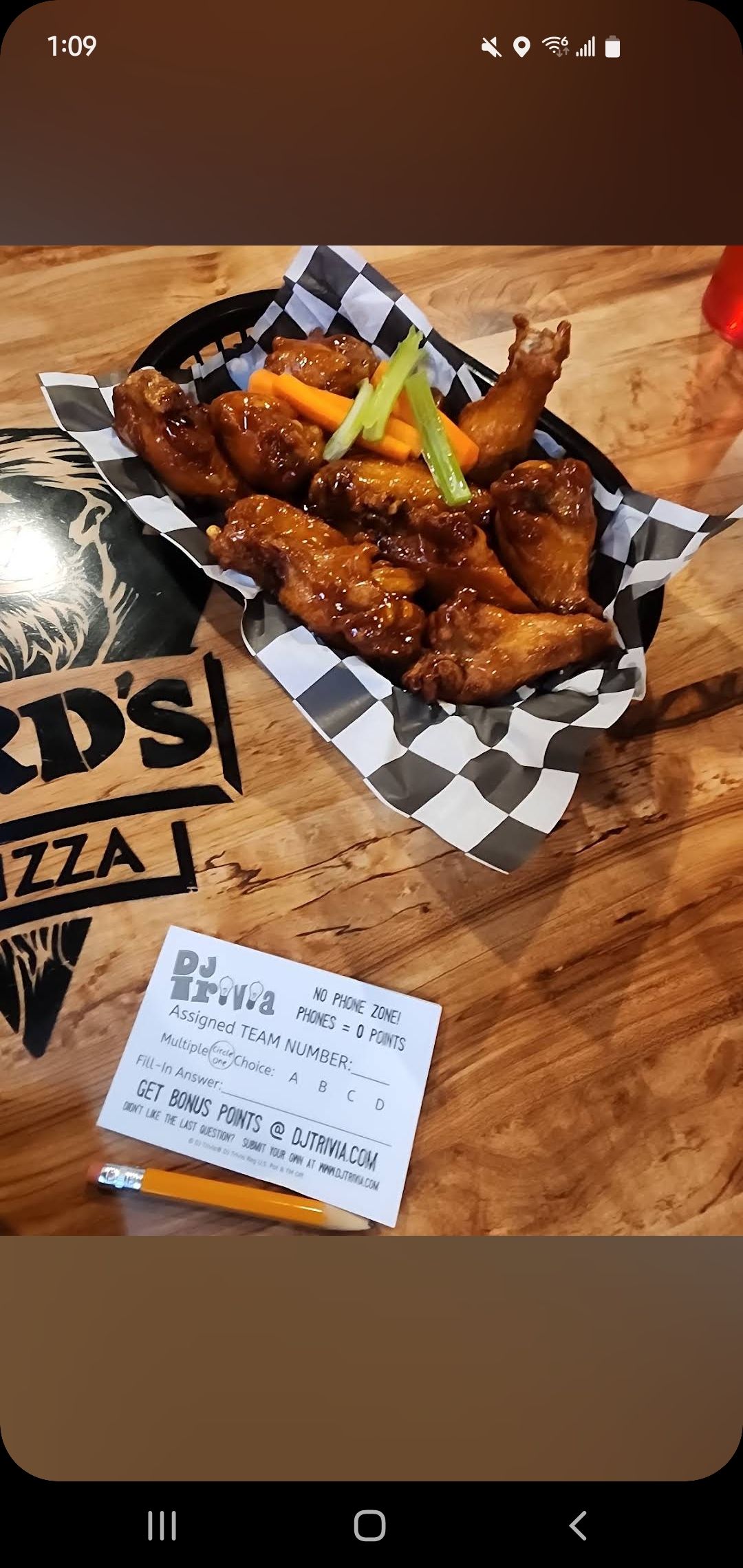 A bowl of chicken wings on a checkered napkin on a wooden table.