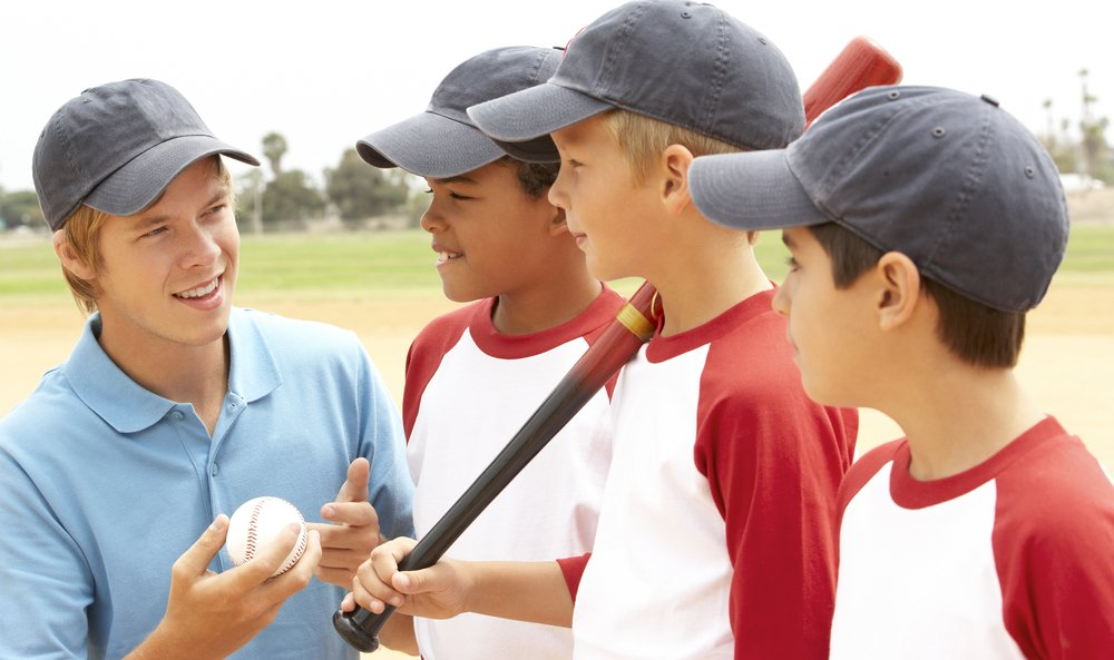 A man is holding a baseball and talking to a group of young boys.