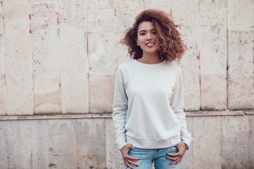 A woman with curly hair is wearing a white sweatshirt and jeans.
