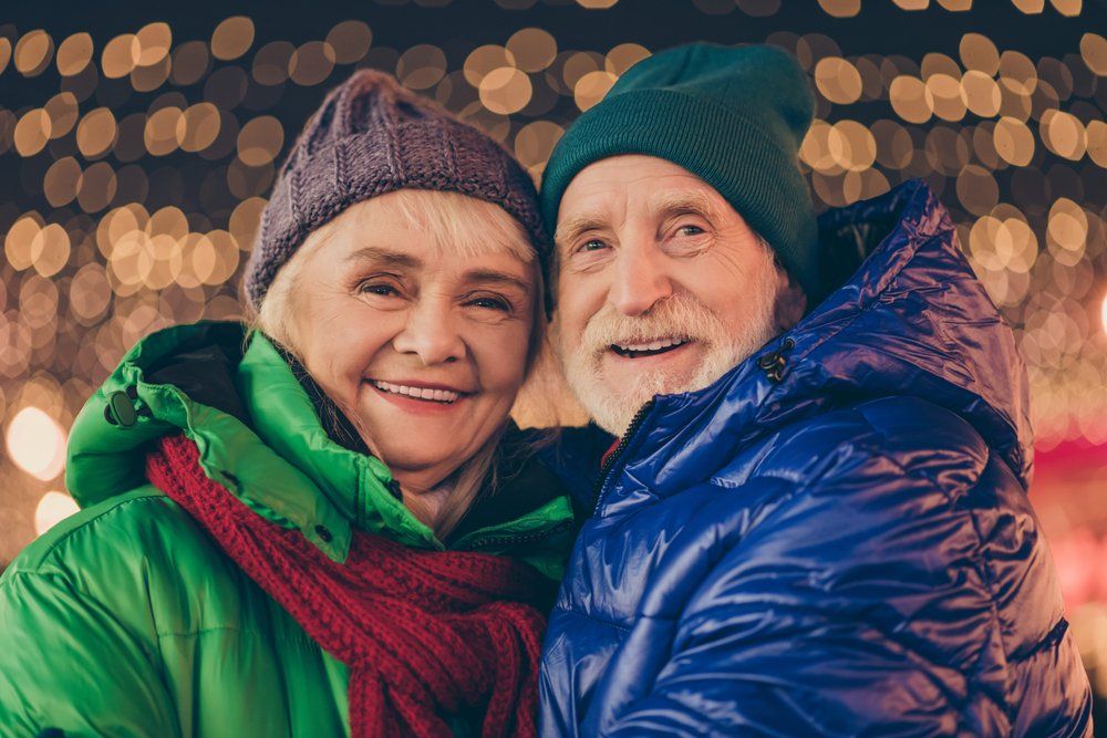 A man and a woman are hugging each other in front of christmas lights.