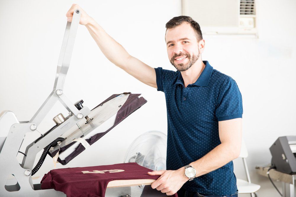 A man is standing in front of a machine that is printing a shirt.