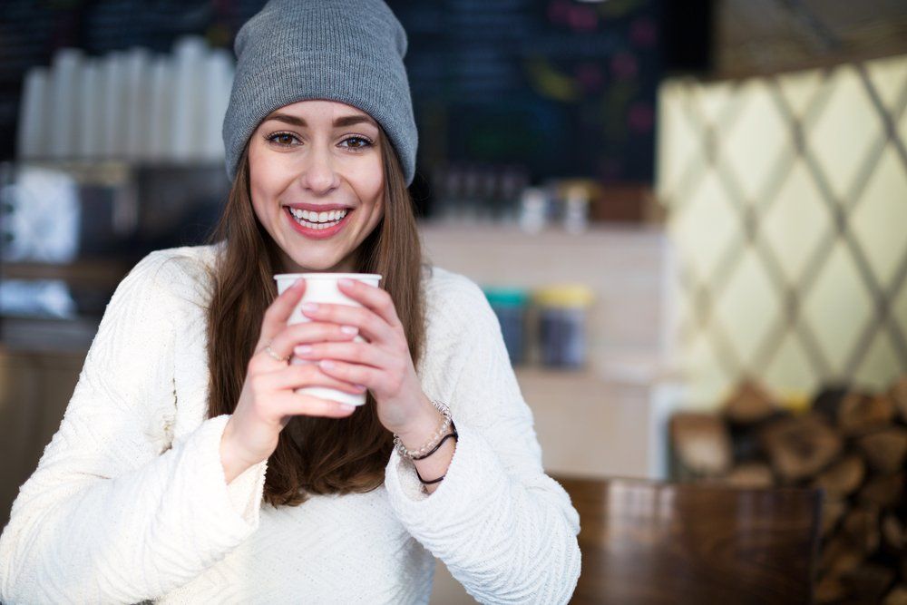 A woman is sitting at a table holding a cup of coffee.
