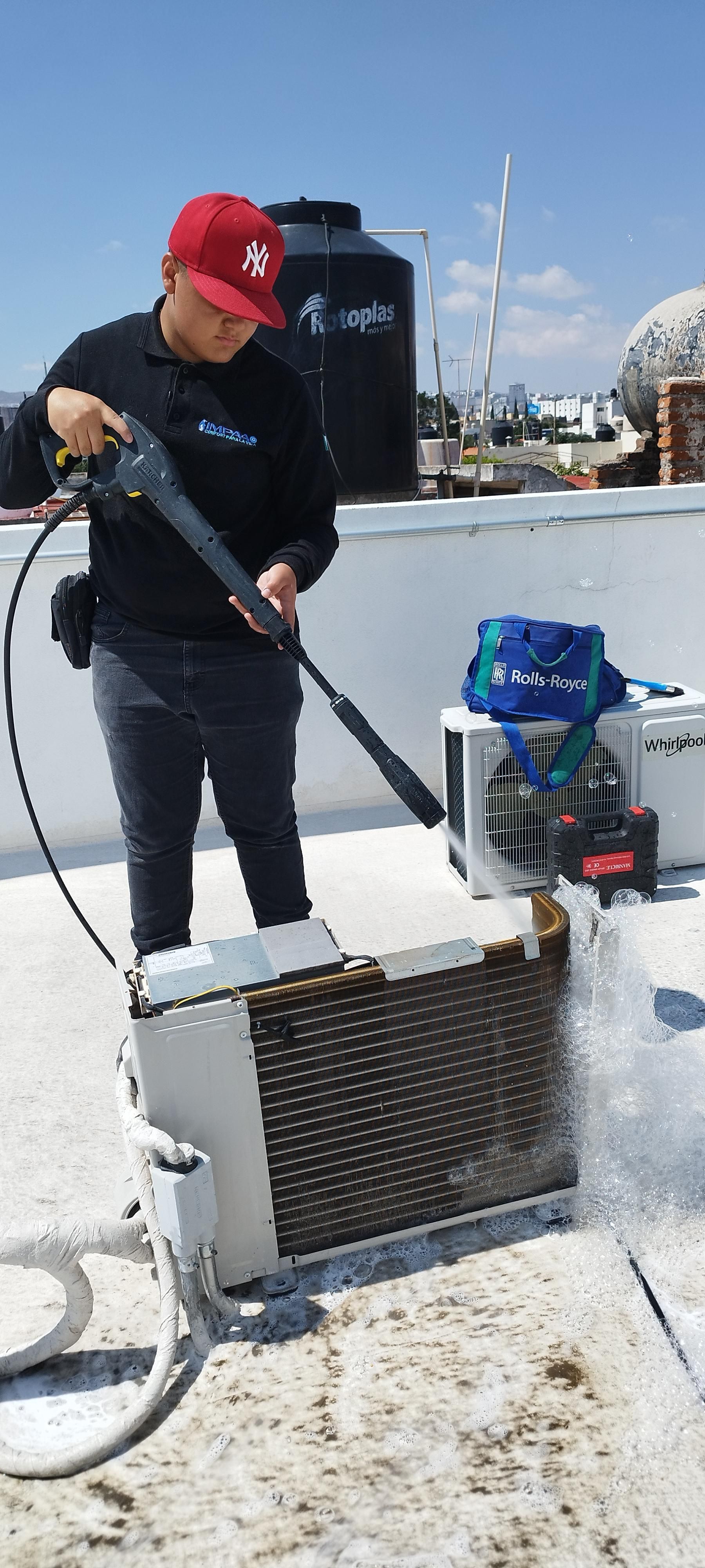 Un operario utiliza una hidrolimpiadora para limpiar las bobinas del condensador de una unidad de aire acondicionado en una azotea plana.