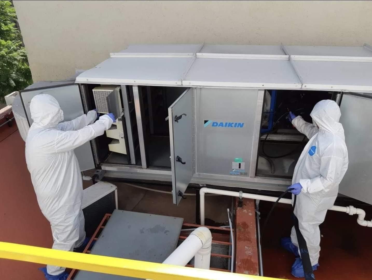 Dos personas con trajes protectores blancos limpian y realizan el mantenimiento de una unidad de climatización industrial Daikin en una azotea.