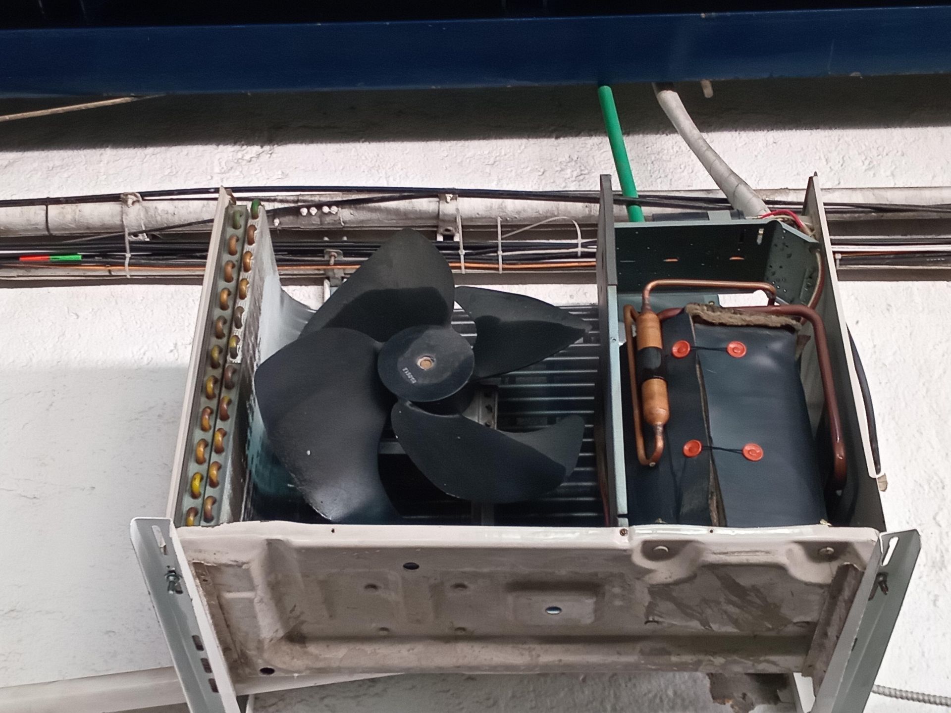 Vista superior de una unidad de aire acondicionado exterior abierta que muestra un ventilador negro, serpentines de cobre y un compresor aislado.