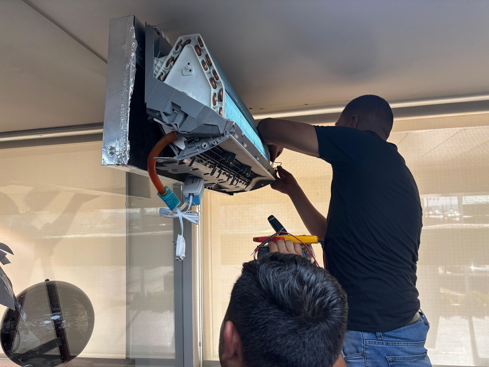 Un técnico trabaja en los componentes internos de una unidad de aire acondicionado mural mientras otra persona observa.