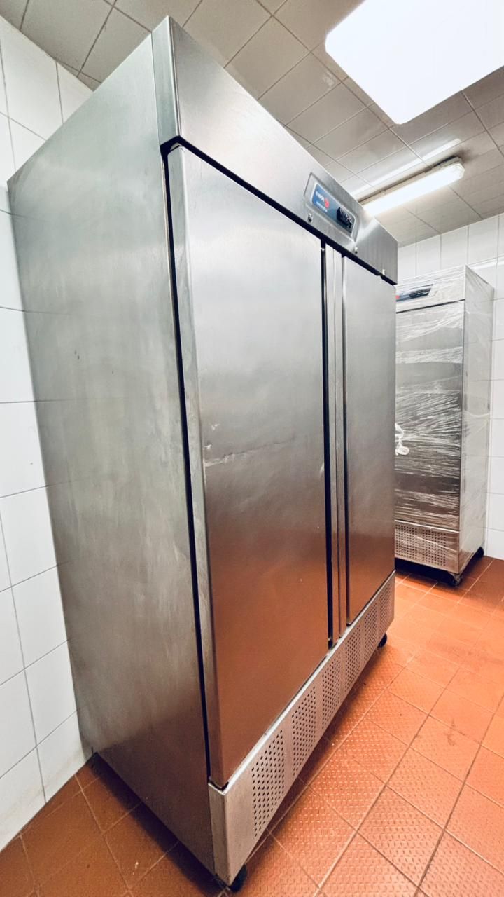 En una cocina con paredes alicatadas y suelo de baldosas naranjas, se encuentra un frigorífico comercial de dos puertas de acero inoxidable.